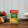 A box of Zatarain'S Garlic Parmesan Long Grain White Rice, 6.9 Oz, is displayed on a rustic wooden table surrounded by fresh ingredients like bell peppers and garlic.