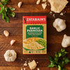 A box of Zatarain'S Garlic Parmesan Long Grain White Rice, 6.9 Oz, is displayed on a wooden surface, surrounded by its fresh ingredients, including whole garlic bulbs, cloves, a wedge of Parmesan cheese, and fresh parsley.