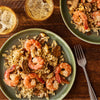 Two green plates are filled with a savory meal of shrimp and mushrooms made with Zatarain'S Garlic Parmesan Long Grain White Rice, 6.9 Oz, set on a wooden table with drinks.