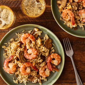 Two green plates are filled with a savory meal of shrimp and mushrooms made with Zatarain'S Garlic Parmesan Long Grain White Rice, 6.9 Oz, set on a wooden table with drinks.