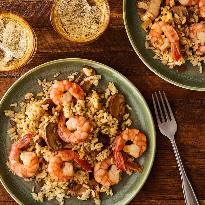 Two green plates are filled with a savory meal of shrimp and mushrooms made with Zatarain'S Garlic Parmesan Long Grain White Rice, 6.9 Oz, set on a wooden table with drinks.