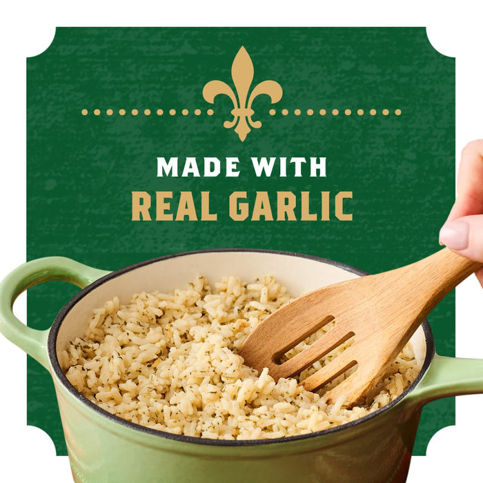 A hand stirs a pot of cooked Zatarain'S Garlic Parmesan Long Grain White Rice, 6.9 Oz with a wooden spoon, shown in front of a green label that reads Made With Real Garlic.