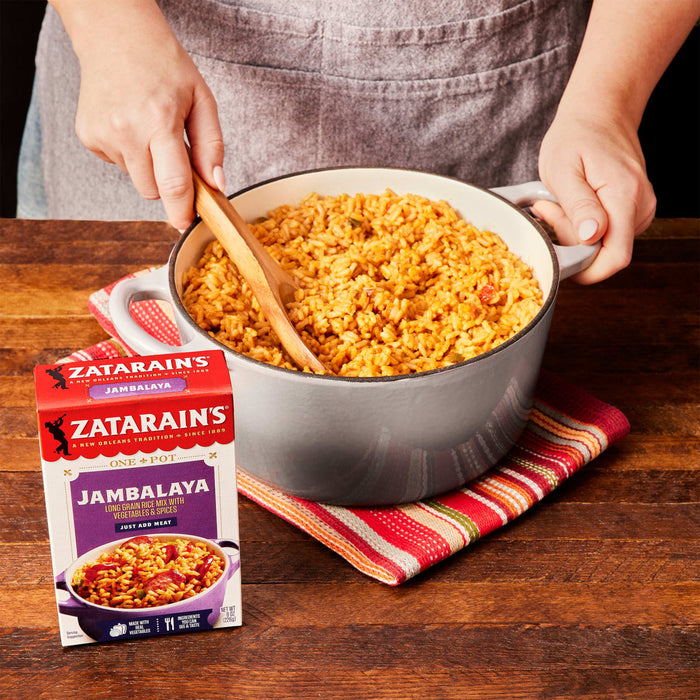 A person is holding a pot of Zatarain's Jambalaya with a wooden spoon.