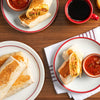 Three breakfast burritos on white plates with red trim one with salsa and one with coffee.