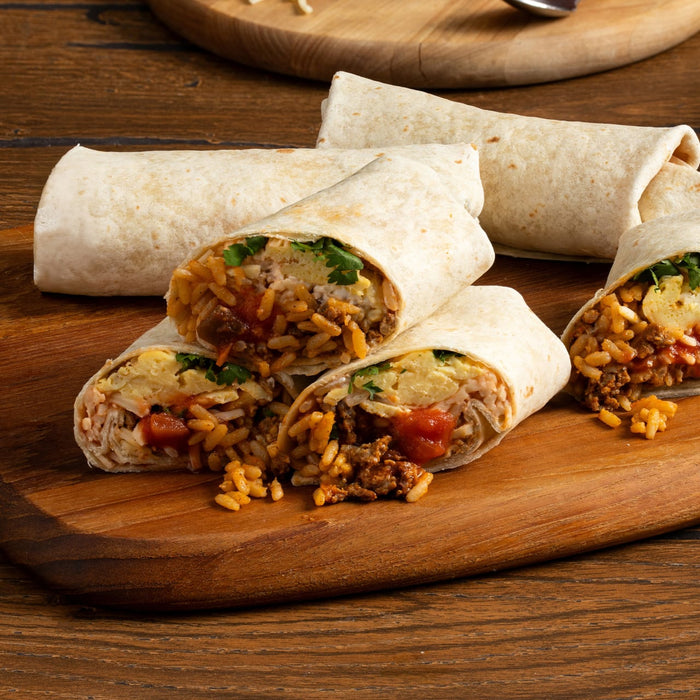 A wooden cutting board displays several breakfast burritos filled with rice meat eggs and salsa some cut open to show the ingredients.