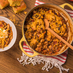 Overhead shot of a yellow pot filled with chicken and rice casserole topped with melted cheese, served with cornbread and a bowl of the casserole garnished with sour cream and shredded cheese.