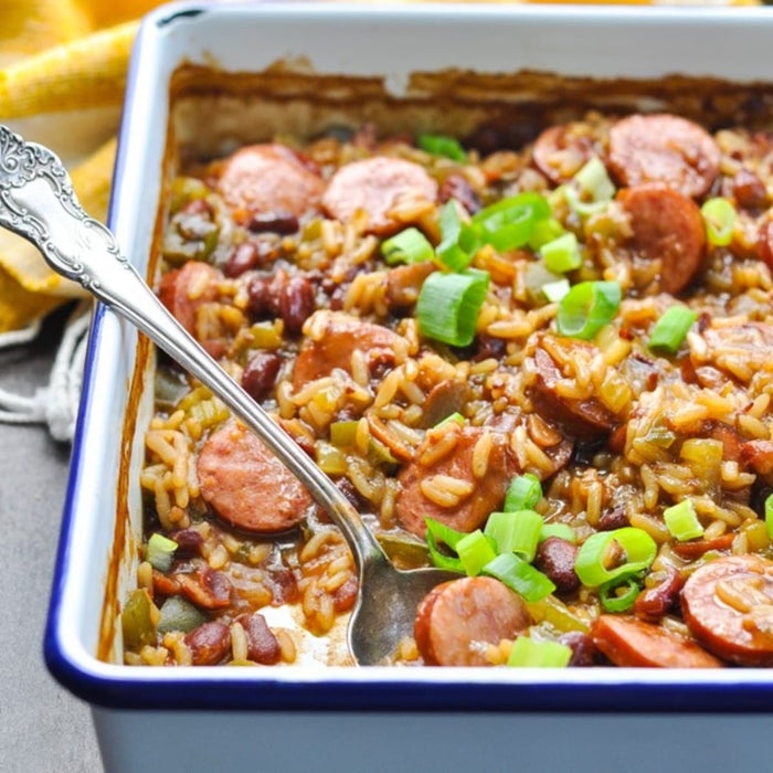 A close-up shot of a casserole dish filled with rice, beans, sausage, and green onions, with a spoon resting inside.
