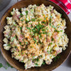 A wooden bowl filled with potato salad, garnished with paprika, parsley, and green onions.