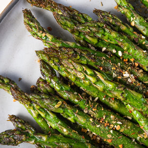 A close up of roasted asparagus spears with herbs and spices.