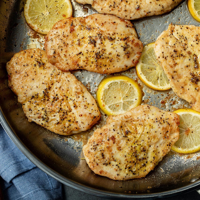A close-up of a pan of cooked chicken breasts with lemon slices.