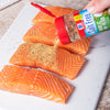 A hand sprinkles McCormick Garlic Salt Free seasoning on salmon fillets.