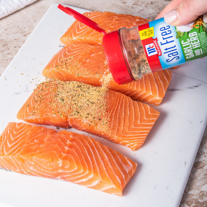 A hand sprinkles McCormick Garlic Salt Free seasoning on salmon fillets.