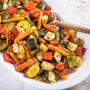 A white plate filled with roasted vegetables, including carrots, zucchini, bell peppers, and squash.