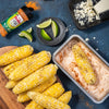 Grilled corn on the cob, lime wedges, and a container of RedHot Chili n Lime seasoning blend.