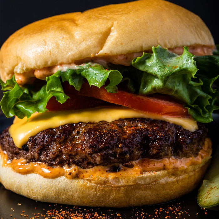 A close-up of a juicy burger with lettuce, tomato, cheese, and a spicy sauce.