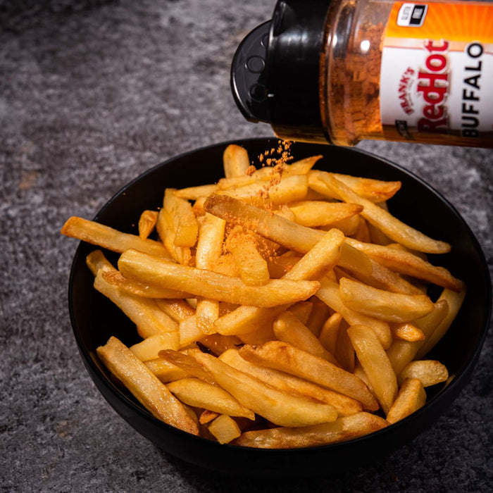 A bowl of french fries being sprinkled with Franks RedHot Buffalo seasoning.