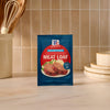 A blue packet of Mccormick Regular Meat Loaf Seasoning Mix 1.25 Oz is displayed on a kitchen countertop, with a utensil holder and a stack of plates in the background.