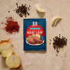 A packet of Mccormick Regular Meat Loaf Seasoning Mix 1.25 Oz is displayed on a countertop surrounded by fresh ingredients like onion, peppercorns, and paprika.