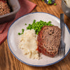 A slice of savory meatloaf, prepared using Mccormick Regular Meat Loaf Seasoning Mix 1.25 Oz, is plated with creamy mashed potatoes and bright green peas for a classic comfort meal.
