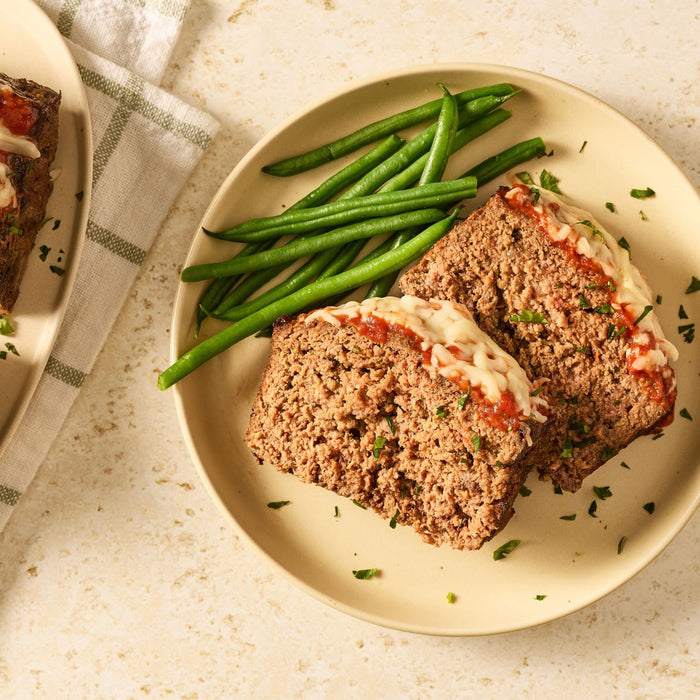 Two slices of meatloaf made with Mccormick Regular Meat Loaf Seasoning Mix 1.25 Oz are served on a plate with green beans.