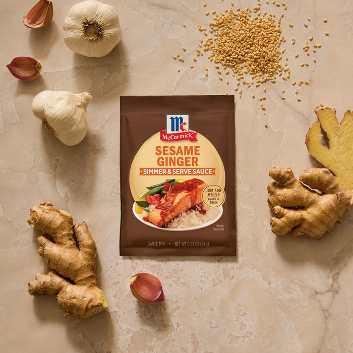 A packet of Mccormick Sesame Ginger All Purpose Sauce Mix Envelope 1 Oz is arranged in a flat lay on a marble surface, surrounded by its fresh ingredients of ginger, garlic, and sesame seeds.