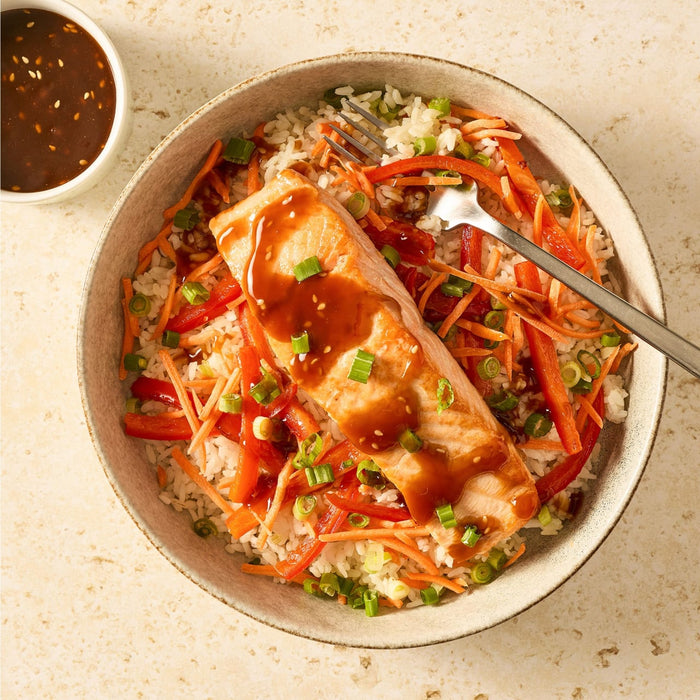 A delicious salmon rice bowl with shredded carrots, red peppers, and green onions is drizzled with a savory sauce made from Mccormick Sesame Ginger All Purpose Sauce Mix Envelope 1 Oz.
