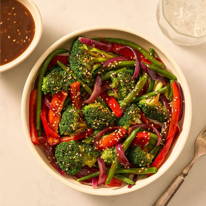 A colorful stir-fry of broccoli, red bell peppers, and green beans is served in a white bowl, a delicious meal that can be made with the Mccormick Sesame Ginger All Purpose Sauce Mix Envelope 1 Oz.
