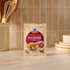 A packet of Mccormick Regular Sauce And Seasoning Mix Envelope 1.5 Oz for Greek Style Gyro with Tzatziki Sauce is displayed on a kitchen counter, next to a utensil holder and a stack of plates.
