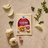 A packet of Mccormick Regular Sauce And Seasoning Mix Envelope 1.5 Oz for Greek Style Gyro is displayed on a countertop surrounded by fresh ingredients like garlic and oregano.