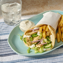A delicious chicken gyro, made with a Mccormick Regular Sauce And Seasoning Mix Envelope 1.5 Oz, is served on a light blue plate with french fries, a side of tzatziki sauce, and a glass of sparkling water.
