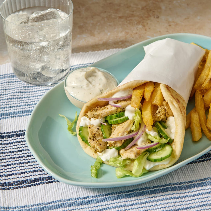 A delicious chicken gyro, made with a Mccormick Regular Sauce And Seasoning Mix Envelope 1.5 Oz, is served on a light blue plate with french fries, a side of tzatziki sauce, and a glass of sparkling water.