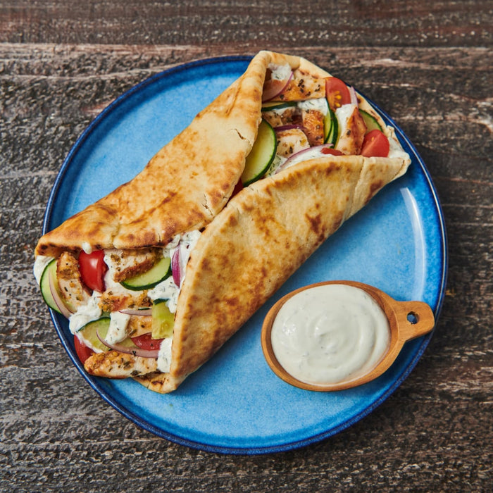 Two chicken gyros, made using a Mccormick Regular Sauce And Seasoning Mix Envelope 1.5 Oz, are presented on a blue plate with a side of creamy dipping sauce.
