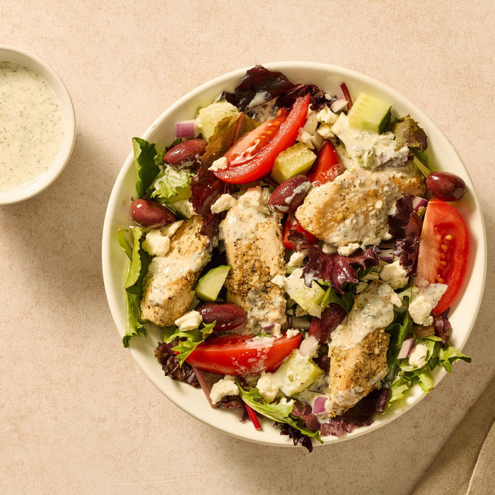 A fresh Greek salad with grilled chicken, tomatoes, and olives is topped with a creamy dressing that can be made using a Mccormick Regular Sauce And Seasoning Mix Envelope 1.5 Oz.