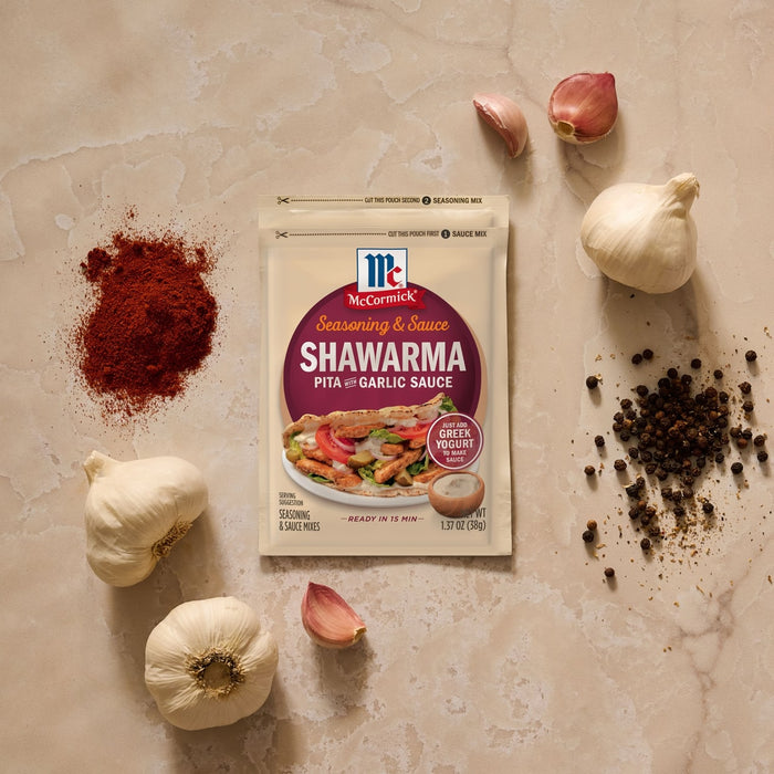 A flat lay product shot shows a Mccormick Regular Sauce And Seasoning Mix Envelope 1.37 Oz for Shawarma, surrounded by ingredients like garlic, paprika, and black peppercorns.