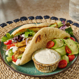 Two freshly prepared chicken pitas, seasoned using Mccormick Regular Sauce And Seasoning Mix Envelope 1.37 Oz, are plated with a side salad and a bowl of creamy dipping sauce.