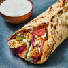 A close-up of a delicious-looking pita wrap, filled with chicken seasoned using Mccormick Regular Sauce And Seasoning Mix Envelope 1.37 Oz, fresh vegetables, and a creamy white sauce.