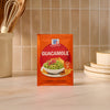 A bright orange packet of Mccormick Regular Seasoning Mix 1 Oz for guacamole is centered on a kitchen countertop.