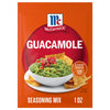 An orange packet of Mccormick Regular Seasoning Mix 1 Oz for guacamole sits behind a white bowl of freshly made guacamole with tortilla chips.