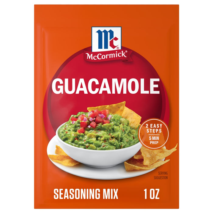 An orange packet of Mccormick Regular Seasoning Mix 1 Oz for guacamole sits behind a white bowl of freshly made guacamole with tortilla chips.