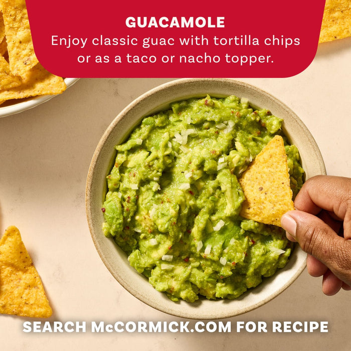 A hand dips a tortilla chip into a bowl of fresh guacamole made with Mccormick Regular Seasoning Mix 1 Oz.