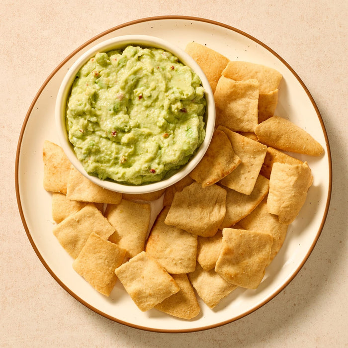 A fresh bowl of guacamole, prepared using Mccormick Regular Seasoning Mix 1 Oz, is presented on a plate with a side of crackers for dipping.
