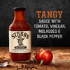 A bottle of Stubbs Original BBQ Sauce with tomatoes black pepper and a wooden background.