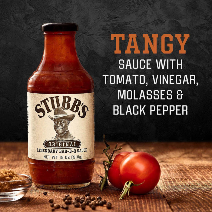 A bottle of Stubbs Original BBQ Sauce with tomatoes black pepper and a wooden background.
