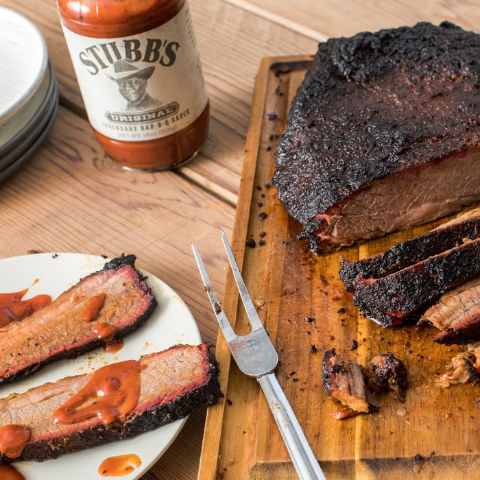 A plate of sliced brisket with Stubbs BBQ sauce a bottle of Stubbs BBQ sauce and a carving fork.