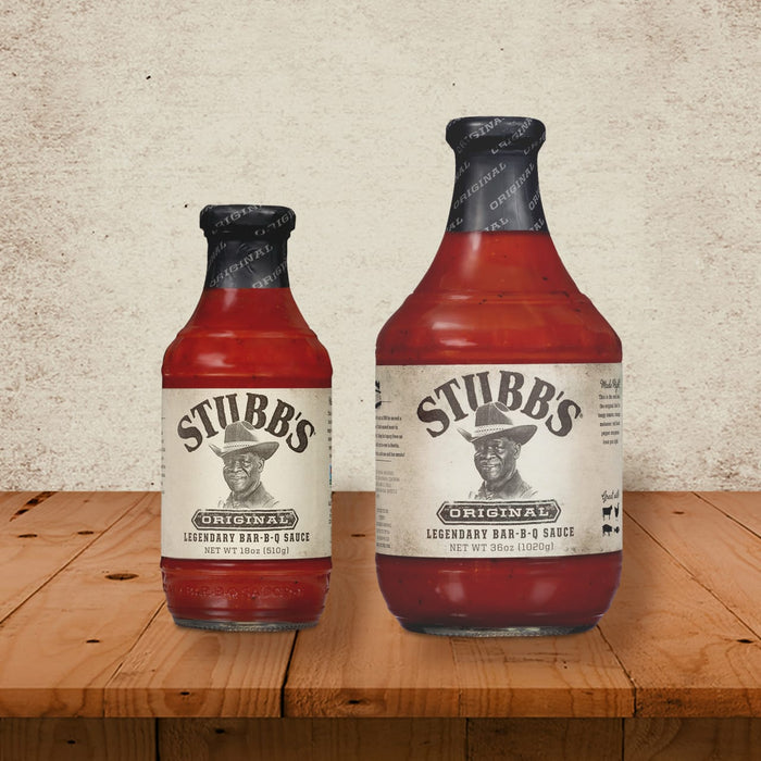 Two bottles of Stubbs Original Legendary Bar-B-Q Sauce one large and one small are on a wooden table.