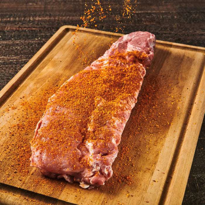 A raw pork chop seasoned with spices on a wooden cutting board.