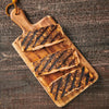 Three pieces of grilled salmon on a wooden cutting board.