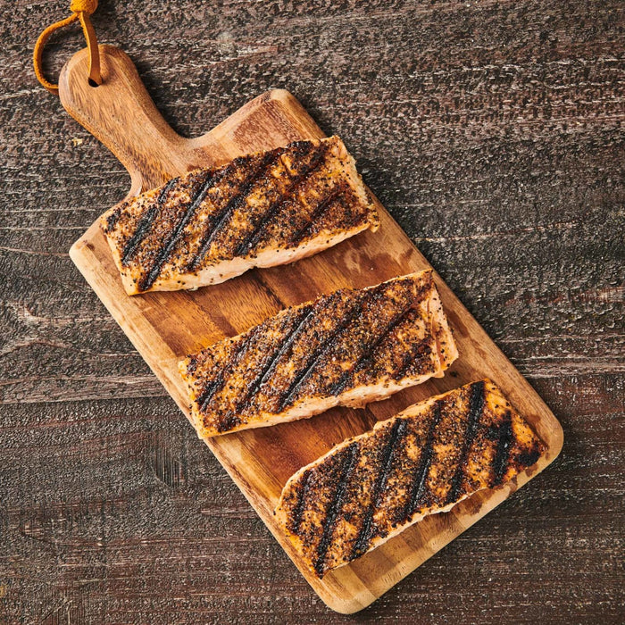 Three pieces of grilled salmon on a wooden cutting board.