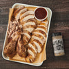 A white tray with sliced and whole turkey breast seasoned with Stubbs Black Pepper Smoke Rub, a small bowl of barbecue sauce, and a bottle of Stubbs Black Pepper Smoke Rub.