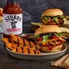A bottle of Stubb's Bar-B-Q Sauce is featured next to two appetizing burgers with sweet potato wedges.